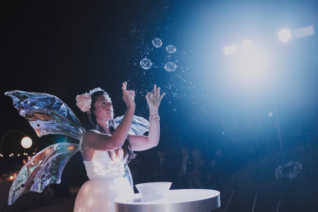 Uno spettacolo di bolle di sapone con abiti luminosi può essere un’esperienza visivamente affascinante e divertente. Questo tipo di spettacolo combina la magia delle bolle di sapone con l’aggiunta di abiti o costumi che emettono luce o che sono decorati con luci luminose.

Immagina un artista delle bolle di sapone che indossa un abito che si illumina al buio o che ha luci integrate al suo interno. Mentre soffia bolle di sapone, queste potrebbero riflettersi e trasmettere la luce emessa dall’abito, creando un effetto straordinario. Le bolle potrebbero sembrare sospese nel vuoto, come sfere luminose che danzano nell’aria.